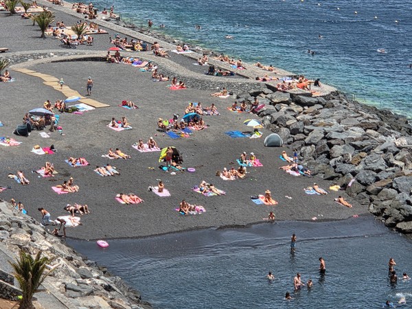 Bañistas en Radazul Playa de Radazul llena de bañistas disfrutando del sol sobre la arena negra protegida por escolleras.